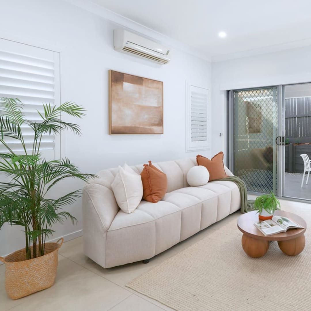 Neutral investment property living room furnished with a sofa, plants and warm accent cushions